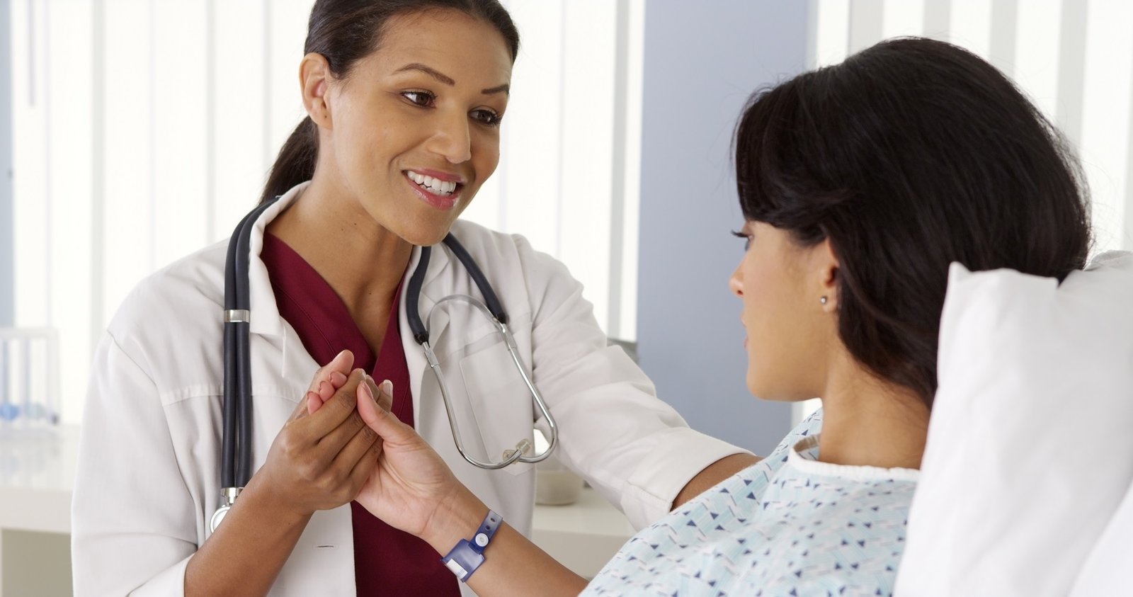 Female doctor holding Hispanic woman's hand and talking